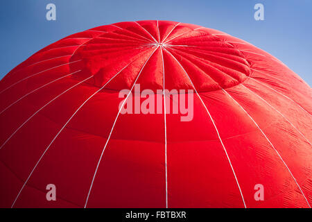 Red canopy of hot air balloon being inflated against a bright blue sky Stock Photo