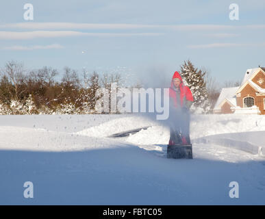 Senior man in red coat using a snow blower during a blizzard on home drive Stock Photo