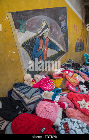 A vast array of colorful colourful knitted woolen hats on a stall.  Behind a large yellow Maaza Gold Tea blend wall mural. Stock Photo