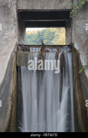 Waters streams over the spillway of a small concrete dam that blocks Hartman Creek and forms a small lake. Stock Photo