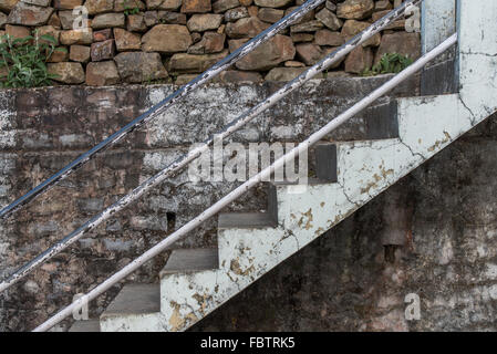 Weathered white paintwork on concrete stairs and mottled wall.  Peeling paint and plaster. Exposed and flaking. Stone wall. Stock Photo