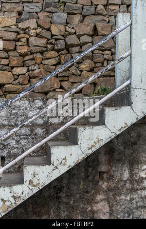 Weathered white paintwork on concrete stairs and mottled wall.  Peeling paint and plaster. Exposed and flaking. Stone wall. Stock Photo