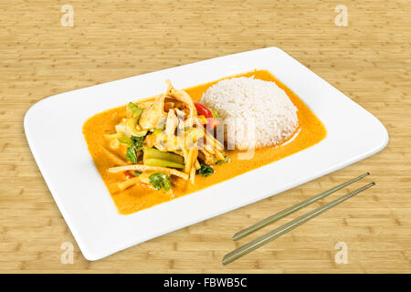 Chinese Food on a white Plate standing on a Table. Roast Chicken with rice, vegetable and coconut sauce. Background Wood. Stock Photo