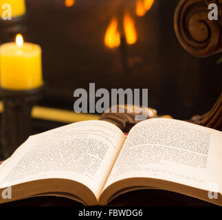 Paperback book open on chair by fire and candle Stock Photo