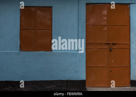 A bold bright blue wall with vibrant orange shuttered window and closed door.  A study of lines and color colour. Stock Photo