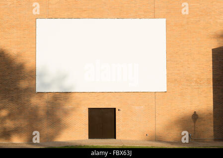 big white blank billboard attached to brown brick wall over a door with shadow Stock Photo