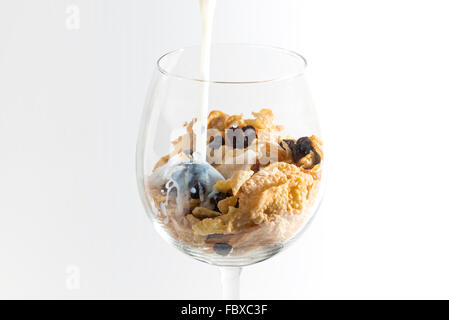wine glass contained cereal and raisin, pouring fresh milk, isolate white background Stock Photo
