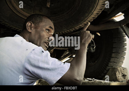 African mechanic under a car checking that everything is ok before entering the desert, Awash, Ethiopia Stock Photo