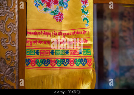Bright yellow hand painted silk scarf detail hung in the small Monastery in town,  Bomdila, Arunachal Pradesh, India. Stock Photo
