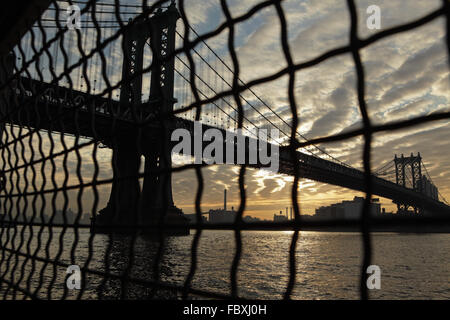 Distorted industrial view of Manhattan Bridge waterfront sunrise New York City through a wire fence Stock Photo