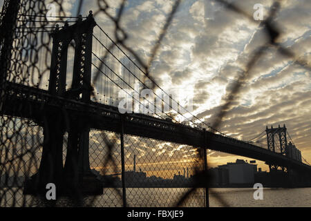 Distorted industrial view of Manhattan Bridge waterfront sunrise New York City through a wire fence Stock Photo