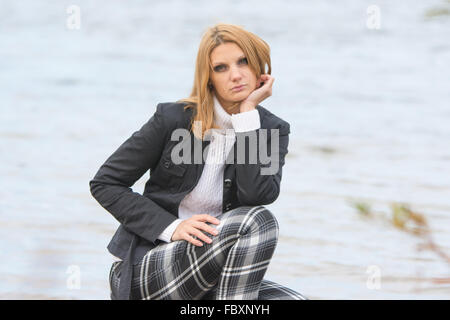 Young beautiful girl sat down by the river in the warm autumn weather Stock Photo