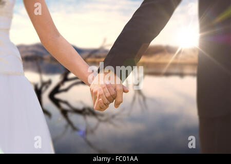 Composite image of mid section of newlywed couple holding hands in park Stock Photo