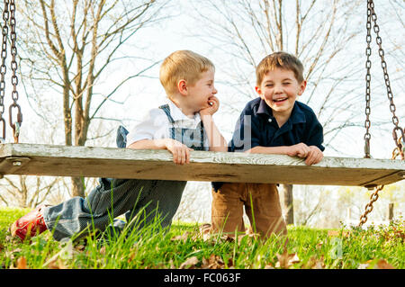 Two boys leaning on swing laughing together Stock Photo