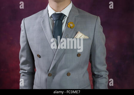 Man in double breasted grey suit, plaid texture, blue necktie, flower brooch, and dot pattern handkerchief, close up Stock Photo