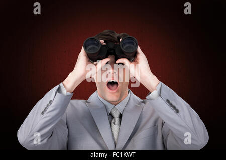 Composite image of suprised businessman looking through binoculars Stock Photo