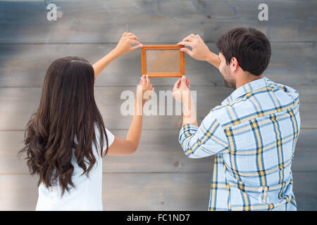 Composite image of happy young couple putting up picture frame Stock Photo