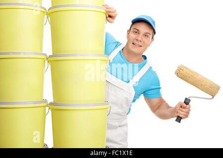 Young male decorator holding a paint roller and posing behind a stack of color buckets isolated on white background Stock Photo