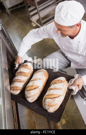 Baker taking tray of fresh bread out of oven Stock Photo