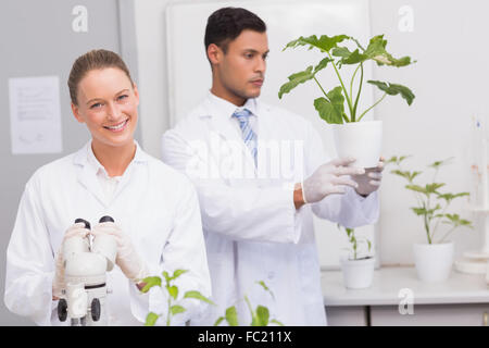 Scientist smiling at camera while colleague looking at plant Stock Photo