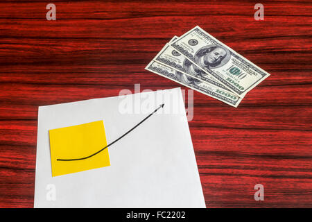 Curve graph printed on a sheet of paper and yellow note pointing a dollar bills. Stock Photo