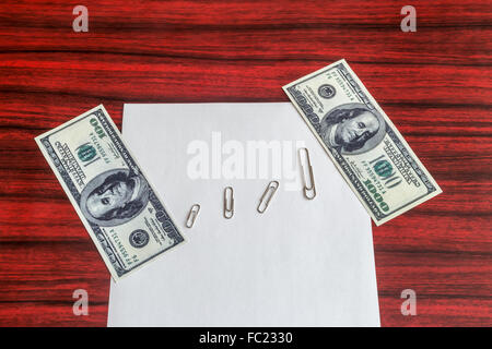 Paper clips arranged by size between 100 and 1000 dollar bill on a sheet of paper Stock Photo