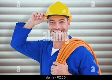 Composite image of confident repairman wearing hard hat while holding wire roll Stock Photo