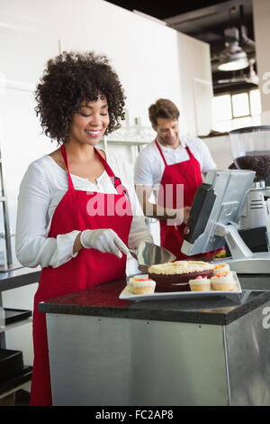 Pretty waitress slicing cake with waiter behind her Stock Photo