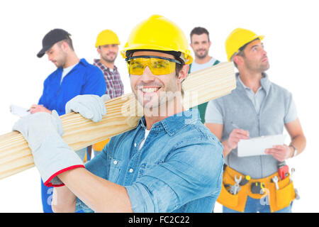 Composite image of carpenter wearing hardhat and glasses while carrying wooden planks Stock Photo