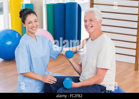 Female instructor with senior man lifting dumbbells Stock Photo