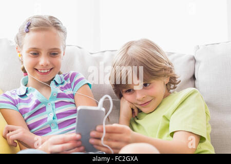 Siblings listening music through mobile phone at home Stock Photo