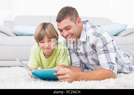 Father and son reading book while lying on floor Stock Photo