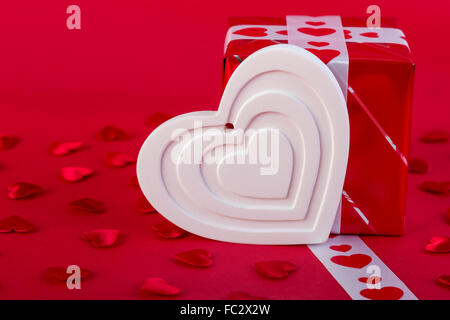 Red Holidays gift and heart on red background. Valentines day background. Stock Photo