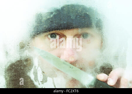 Scary man with knife outside a frozen window in winter Stock Photo