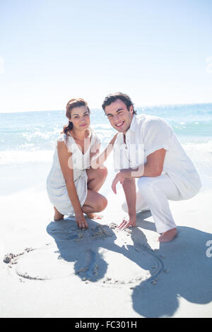 Happy couple drawing heart shape in the sand Stock Photo