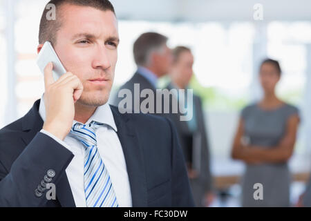 Businessman on the phone with colleagues behind him Stock Photo