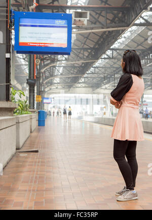 Woman watching the information board on the platform at the train station Stock Photo