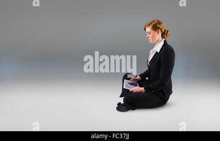 Composite image of redhead businesswoman using her tablet pc Stock Photo