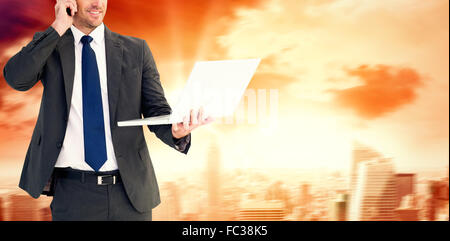 Composite image of businessman talking on phone holding laptop Stock Photo