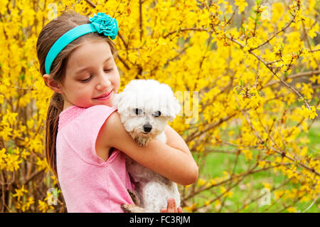 girl holding her dog by forsythia bush Stock Photo