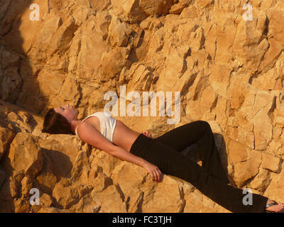 Young lady in good shape wearing yoga clothes relaxing on some rocks in the sunshine after hiking and outdoor yoga in Israel Stock Photo