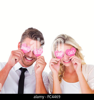 Composite image of attractive young couple holding pink hearts over eyes Stock Photo