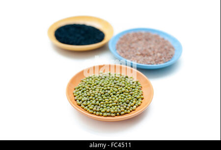 Three coloured bowls with mung green bean seeds close up and two out of focus isolated on white background Stock Photo