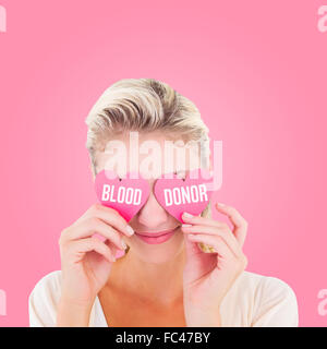 Composite image of attractive young blonde holding hearts over eyes Stock Photo