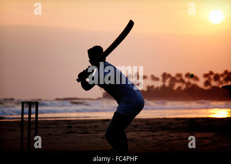 Boy playing cricket at sunset on tropical beach in Sri Lanka Stock Photo