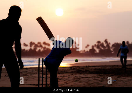 Boy playing cricket at sunset on tropical beach in Sri Lanka Stock Photo