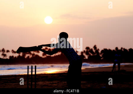 Boy playing cricket at sunset on tropical beach in Sri Lanka Stock Photo