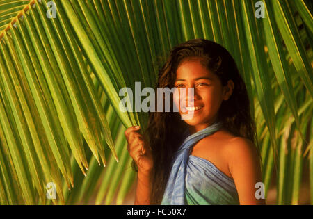 Polynesian girl in front of green palm fronds on Cook Islands in sunset light Stock Photo