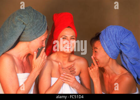 Three women of ethnic mix with colorful bath towels sharing gossip and laughing
