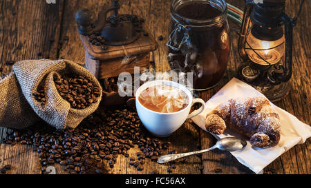 Rural Italian breakfast of coffee and croissant on a wooden table with a kerosene lamp. Stock Photo